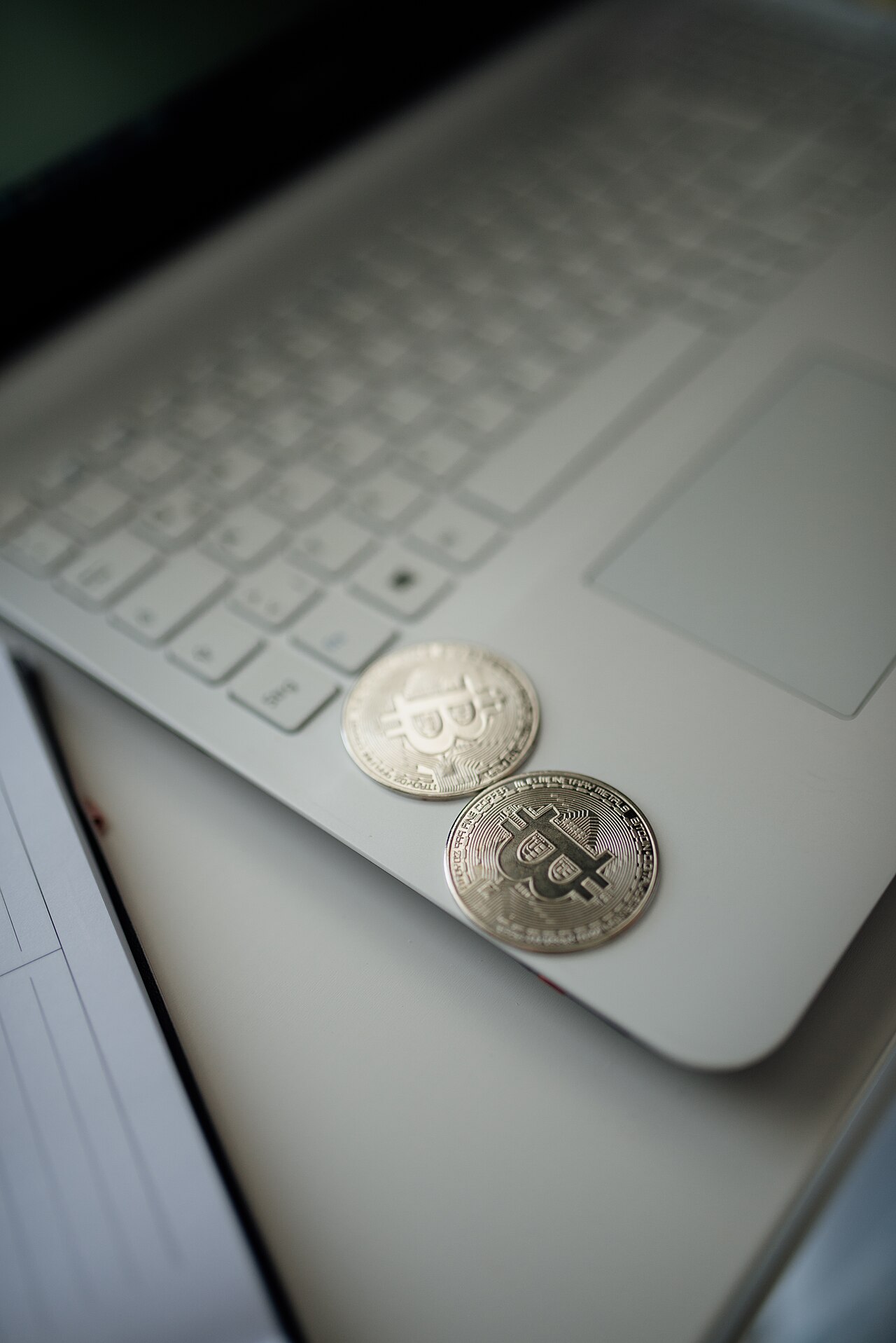 Silver cryptocurrency coins on a laptop keyboard with a notepad in the background in a minimal workspace setting